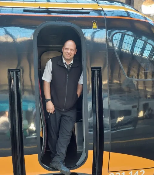 rob-photo-head-shot Counsellor Rob standing in the doorway of a modern train, smiling at the camera.