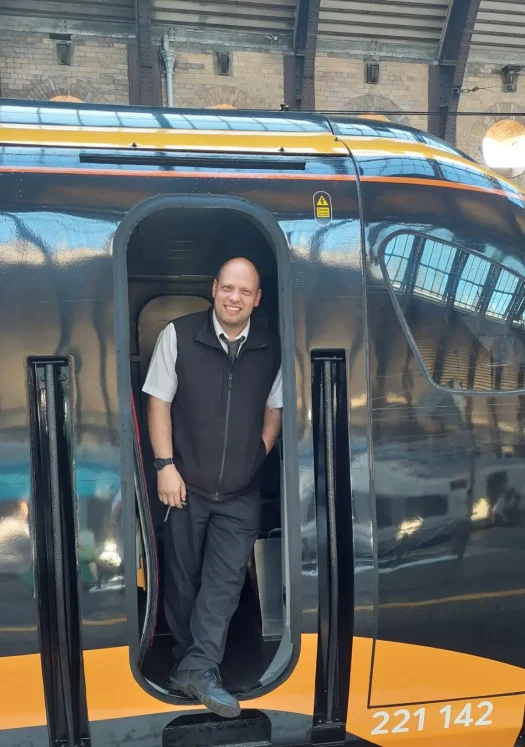 rob-photo-head-shot Counsellor Rob standing in the doorway of a modern train, smiling at the camera.